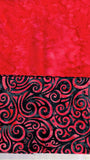 A close-up of a red and black patterned fabric, featuring a solid textured red upper section and a black lower section with a red swirling scrollwork design.