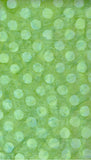 A close-up of a light green textured cotton batik material with a repeating pattern of spots.
