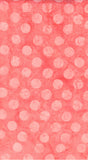 A close-up of a peach pink cotton batik fabric with a repeating pattern of larger and larger light pink polka dots on a coral-pink background.