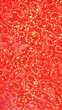 A close-up of an orange cotton batik fabrics covered with many small scattered dots and streaks in yellow, white, and a few pale blue and purple marks.