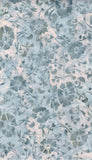 A close-up of a light grey blue and white batik fabric with a repeating floral and vine pattern.