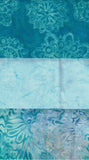 A close-up of a batik fabric with horizontal color bands, featuring teal, light blue, and turquoise patterns with floral and paisley motifs.
