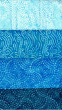 A close-up of layered blue batik fabric strips with different wave and dotted patterns in various shades of light to dark blue.